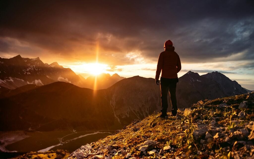 A hiker enjoys a breathtaking sunset view over the dramatic Alpine mountain range.