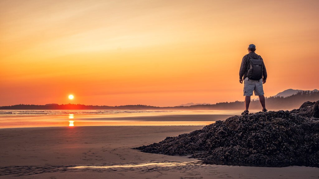 silhouette of man standing on rock near sea during sunset